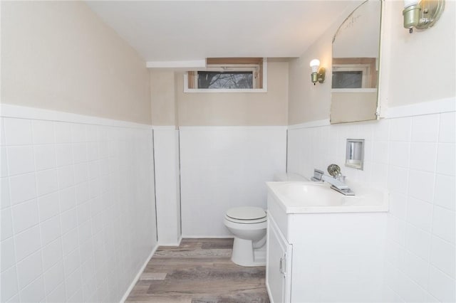 half bathroom with toilet, a wainscoted wall, wood finished floors, vanity, and tile walls