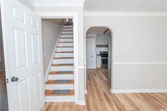 stairs with arched walkways, baseboards, wood finished floors, and crown molding