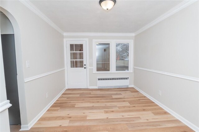 interior space featuring baseboards, arched walkways, radiator, ornamental molding, and light wood-style floors