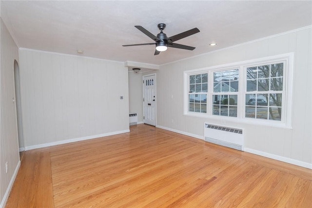 spare room with radiator, light wood-style flooring, arched walkways, and ornamental molding