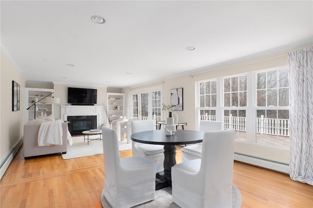 dining area with ornamental molding, a baseboard radiator, a glass covered fireplace, and light wood-style floors