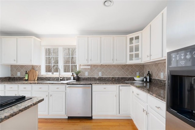 kitchen featuring wall oven, white cabinetry, a sink, dark stone countertops, and dishwasher