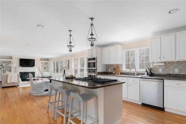 kitchen with white cabinets, light wood-style flooring, appliances with stainless steel finishes, a fireplace, and a sink