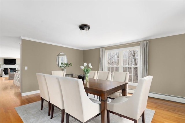 dining area featuring a baseboard heating unit, ornamental molding, light wood-style flooring, and baseboards