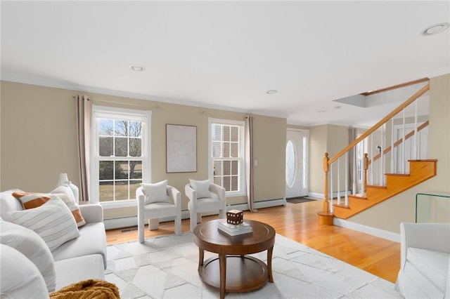 living room featuring a baseboard heating unit, baseboards, light wood-style floors, stairway, and crown molding