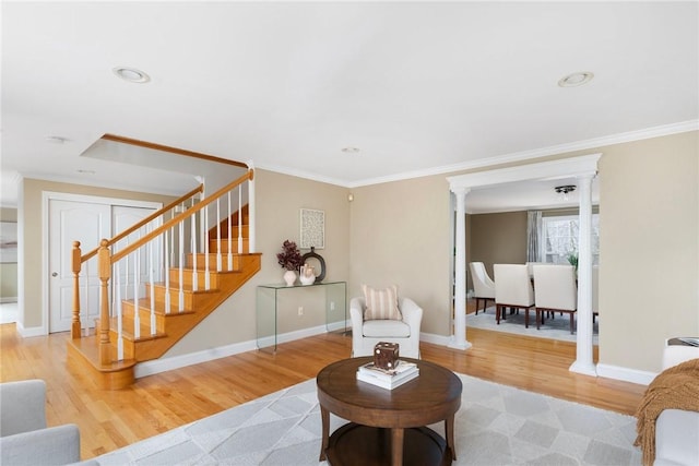 living room featuring decorative columns, baseboards, wood finished floors, stairs, and crown molding