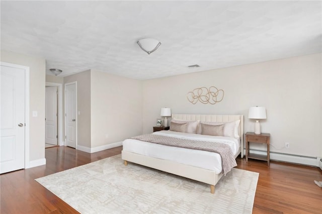 bedroom with a baseboard heating unit, visible vents, baseboards, and wood finished floors