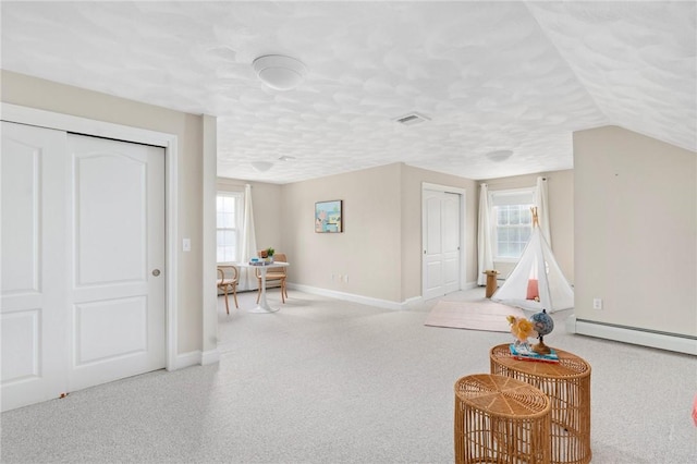 living area featuring a textured ceiling, a baseboard heating unit, carpet flooring, visible vents, and baseboards