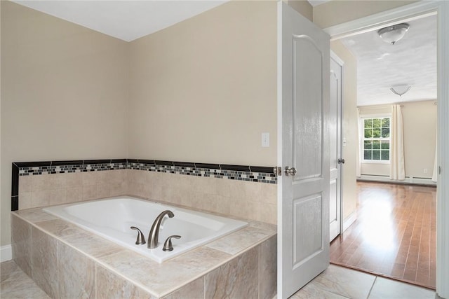 full bath featuring a baseboard heating unit, a garden tub, and wood finished floors