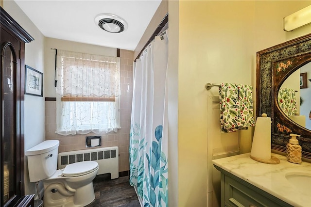 bathroom with visible vents, radiator, toilet, vanity, and tile walls