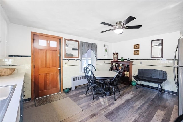 dining room featuring a ceiling fan, wainscoting, radiator, dark wood-style floors, and tile walls