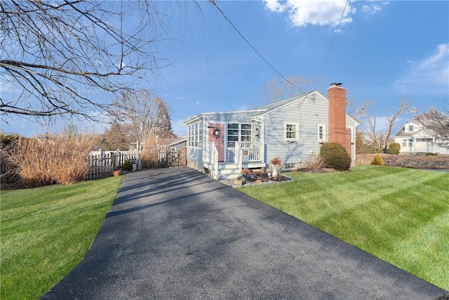 view of side of property with driveway, fence, a chimney, and a lawn