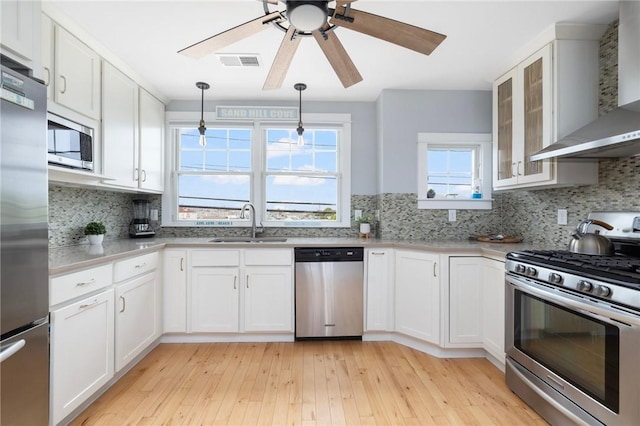 kitchen with visible vents, appliances with stainless steel finishes, white cabinets, a sink, and wall chimney exhaust hood