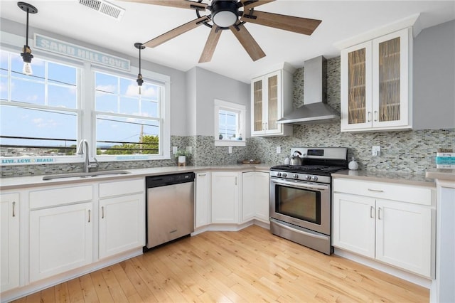 kitchen with light countertops, visible vents, appliances with stainless steel finishes, a sink, and wall chimney exhaust hood