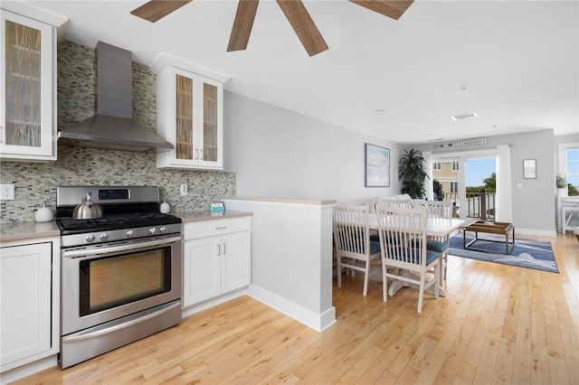 kitchen with backsplash, light wood-style floors, white cabinets, gas range, and wall chimney exhaust hood