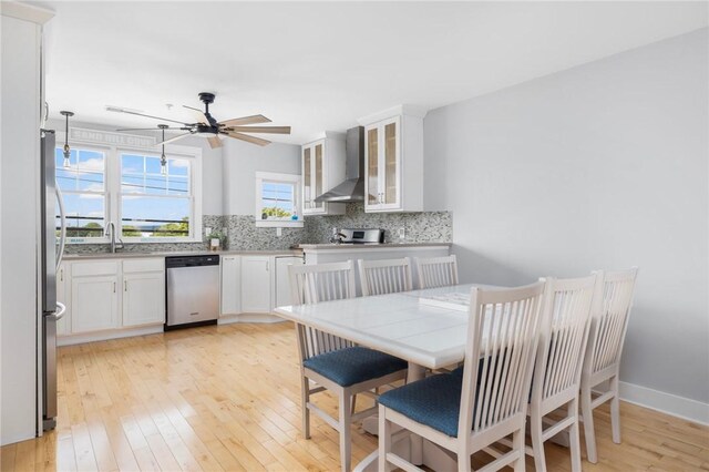 kitchen with tasteful backsplash, light wood-type flooring, wall chimney exhaust hood, and stainless steel appliances