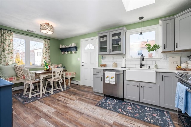 kitchen with stainless steel appliances, backsplash, gray cabinetry, a sink, and wood finished floors