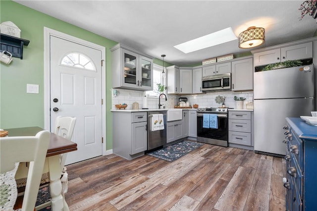 kitchen featuring gray cabinetry, stainless steel appliances, a skylight, a sink, and decorative backsplash