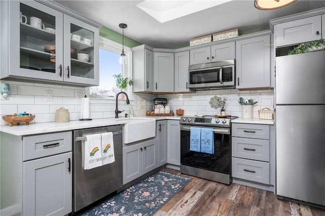 kitchen with appliances with stainless steel finishes, dark wood-type flooring, light countertops, gray cabinetry, and a sink