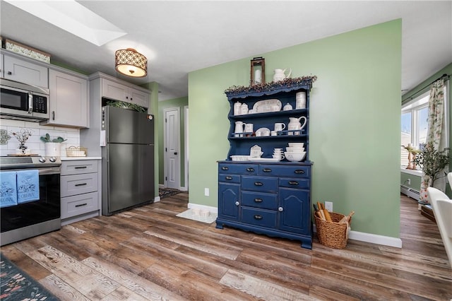 kitchen with baseboards, appliances with stainless steel finishes, backsplash, and dark wood-style flooring