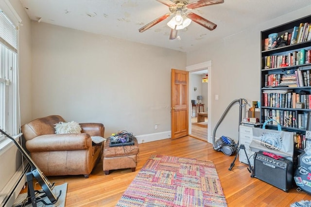 sitting room featuring a baseboard heating unit, ceiling fan, wood finished floors, and baseboards