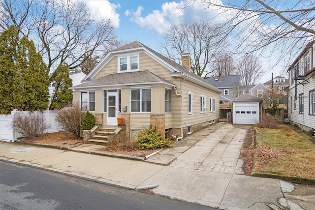 view of front of house with an outbuilding, a detached garage, a chimney, a shingled roof, and concrete driveway