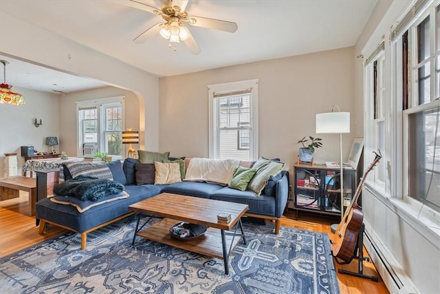 living room featuring a healthy amount of sunlight, a baseboard heating unit, arched walkways, and wood finished floors