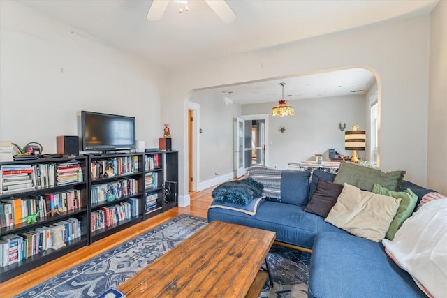 living area featuring baseboards, ceiling fan, arched walkways, and wood finished floors