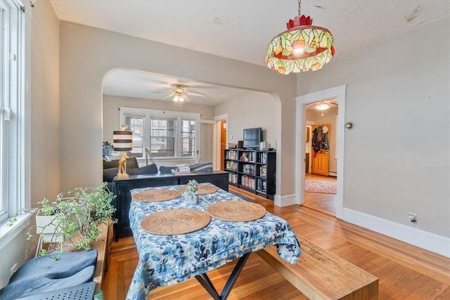 dining room featuring arched walkways, ceiling fan, light wood finished floors, and baseboards