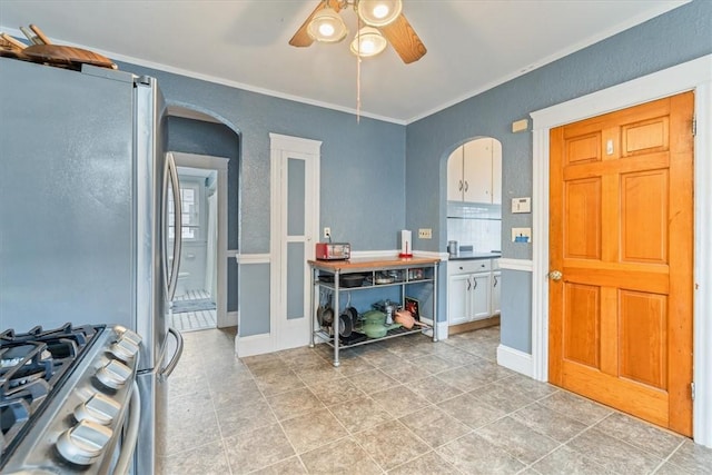 interior space featuring baseboards, arched walkways, a ceiling fan, and ornamental molding