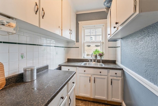 kitchen with a wainscoted wall, dark countertops, a textured wall, white cabinetry, and a sink