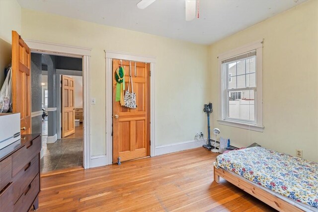 bedroom featuring a ceiling fan, a baseboard radiator, baseboards, and hardwood / wood-style flooring