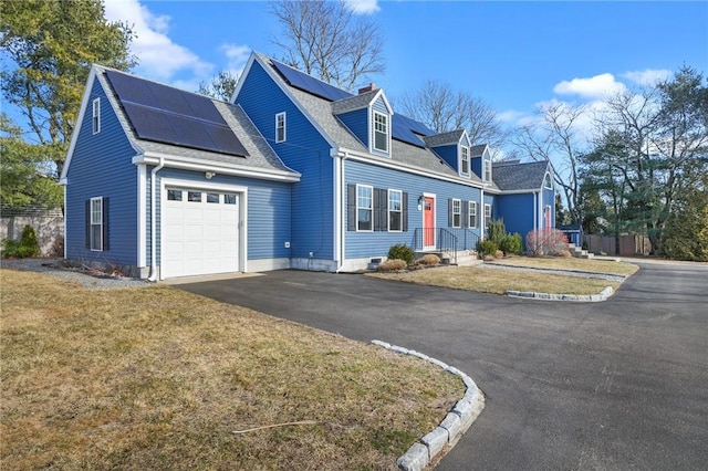 cape cod house with aphalt driveway, a front yard, a shingled roof, a garage, and solar panels