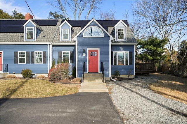 cape cod home featuring solar panels, a shingled roof, gravel driveway, and a front lawn