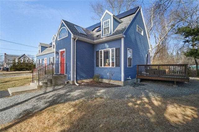 view of front of house featuring a deck, roof mounted solar panels, and roof with shingles