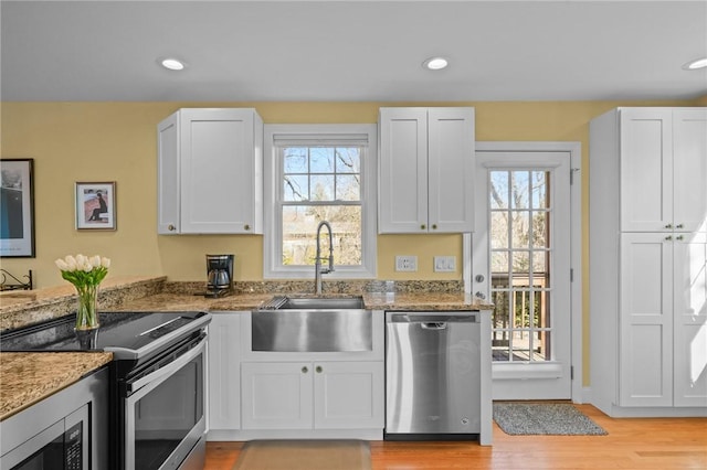 kitchen featuring light wood finished floors, light stone countertops, appliances with stainless steel finishes, and a sink