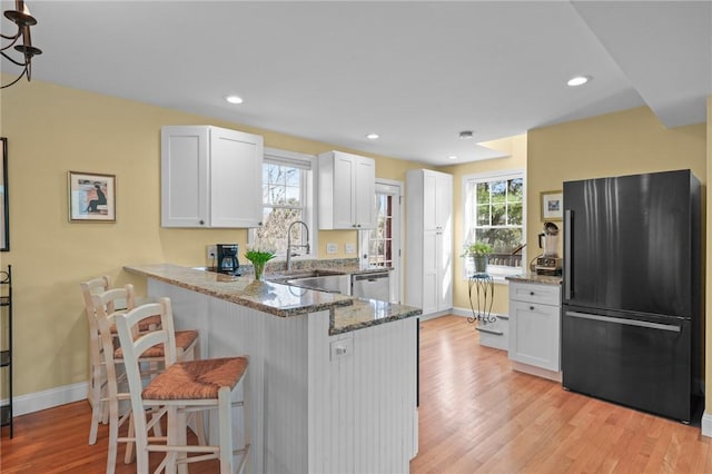 kitchen featuring light wood-type flooring, light stone counters, a peninsula, freestanding refrigerator, and white cabinetry