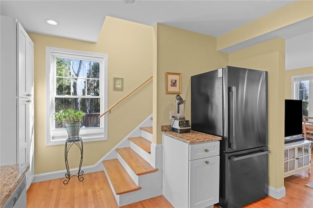 kitchen featuring light stone countertops, white cabinetry, freestanding refrigerator, dishwasher, and light wood-type flooring