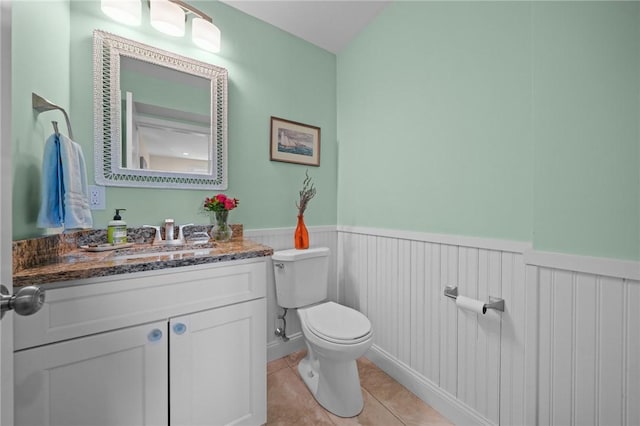 half bath featuring tile patterned flooring, toilet, vanity, and a wainscoted wall