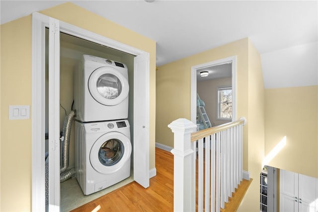 clothes washing area with laundry area, stacked washer and dryer, light wood-style floors, and baseboards