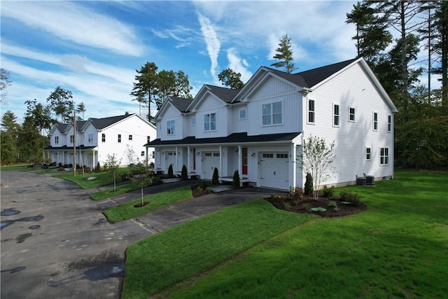 view of front facade with an attached garage, central AC unit, board and batten siding, a front yard, and a residential view