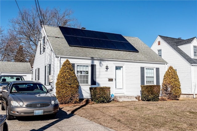 cape cod home featuring roof mounted solar panels and a shingled roof