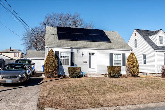 cape cod home with an outbuilding, roof mounted solar panels, a front lawn, and roof with shingles