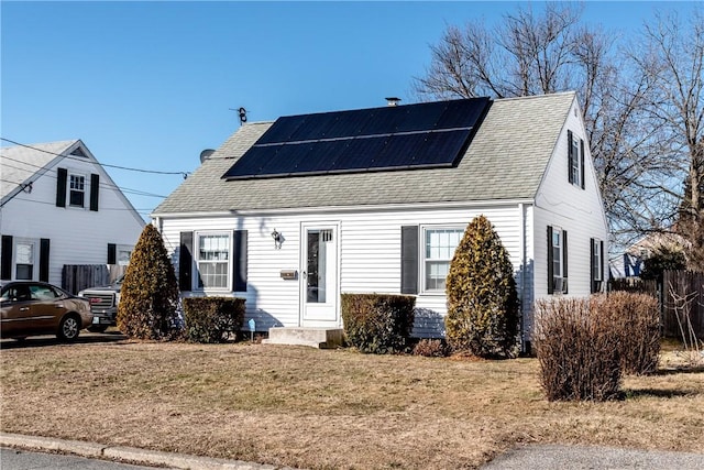 view of front of house featuring a front yard, roof mounted solar panels, and a shingled roof