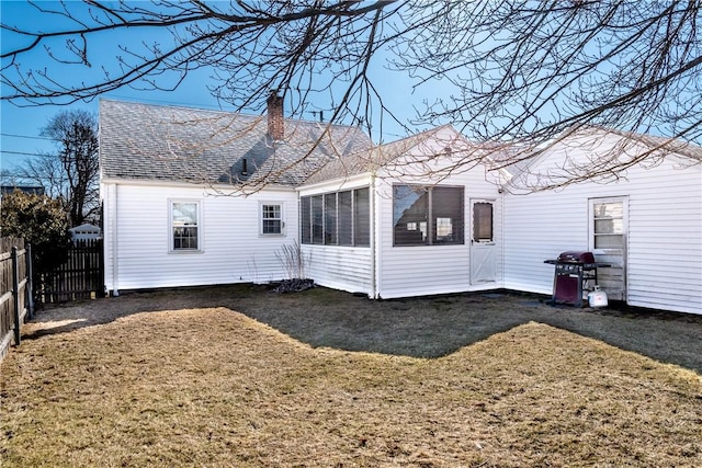 back of house with a lawn, a chimney, roof with shingles, and fence