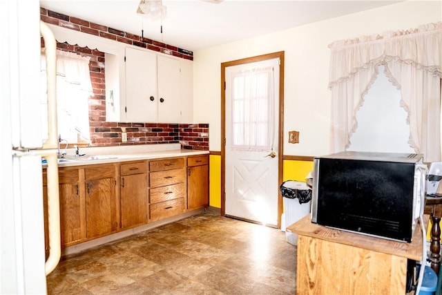 kitchen with a sink, brown cabinets, freestanding refrigerator, and light countertops