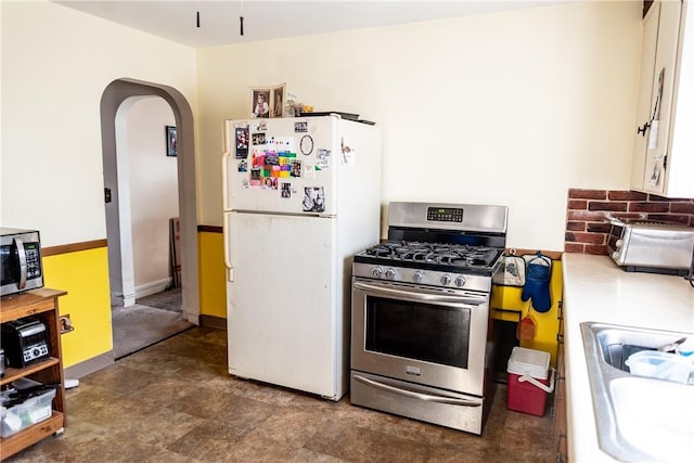 kitchen with baseboards, arched walkways, a sink, light countertops, and appliances with stainless steel finishes