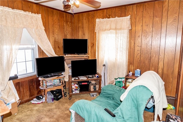 living room with wooden walls, ceiling fan, crown molding, and carpet