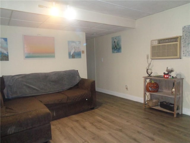 living room featuring a paneled ceiling, baseboards, wood finished floors, and a wall mounted AC