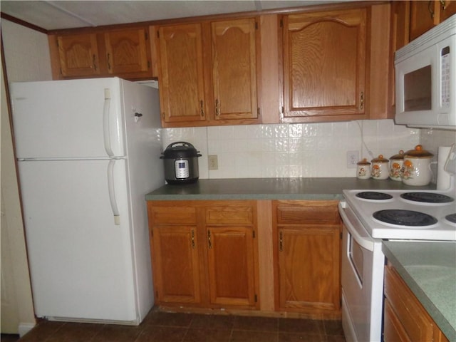 kitchen with brown cabinetry, dark tile patterned flooring, white appliances, and tasteful backsplash